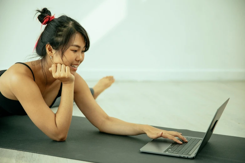 a woman laying on a yoga mat using a laptop, inspired by helen huang, pexels contest winner, looking across the shoulder, south east asian with long, avatar image, sarcastic pose