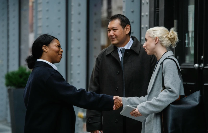 a couple of people that are shaking hands, by Matt Stewart, exterior shot, mix of ethnicities and genders, late morning, professional work