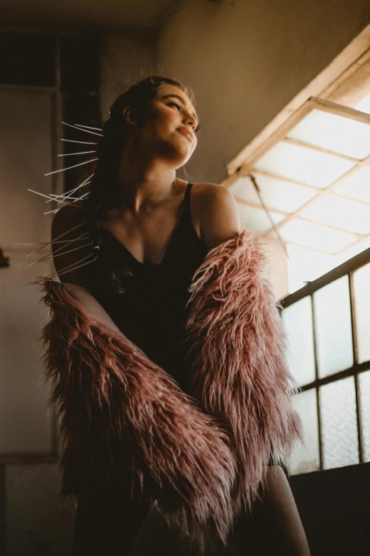 a woman standing in front of a window, a portrait, inspired by Elsa Bleda, trending on pexels, pink fur, feathers growing from arms, satisfied pose, with dramatic lighting