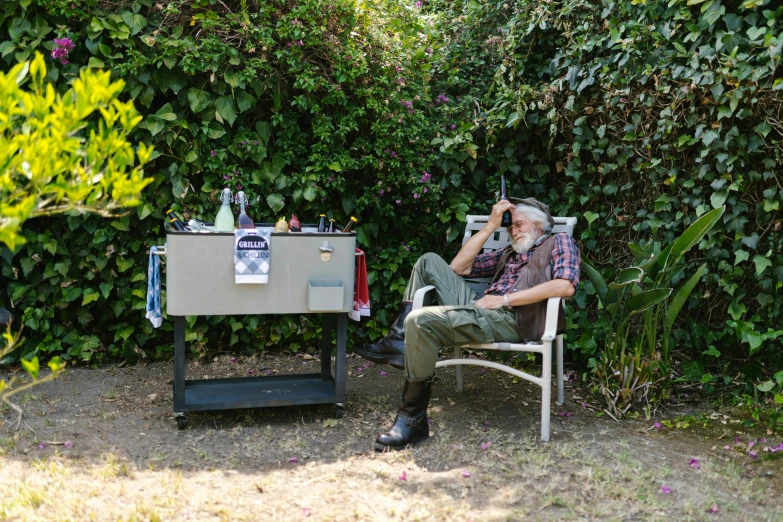 a man sitting in a chair next to a cooler, a portrait, unsplash, plein air, old gigachad with grey beard, mechabot, james web telescope, in the garden