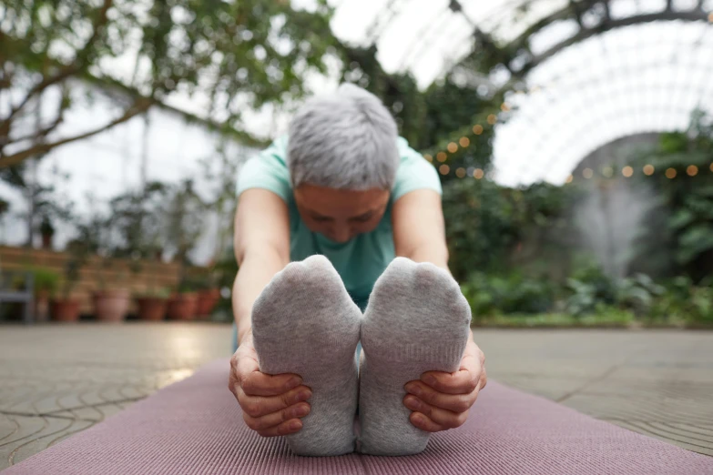 a woman doing a yoga pose on a yoga mat, by Rachel Reckitt, pexels contest winner, an elderly, foot, grey, illuminated
