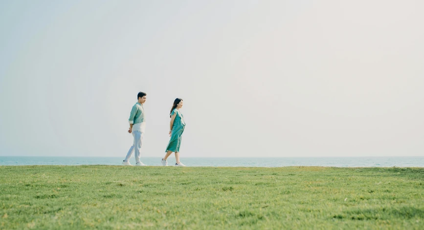 a man and a woman walking across a lush green field, by Jang Seung-eop, pexels contest winner, sea - green and white clothes, pregnant, at the seaside, asian man