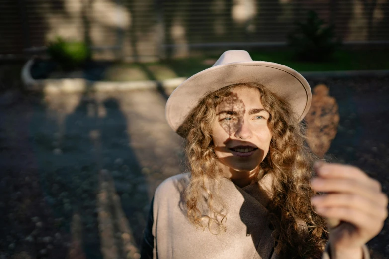 a close up of a person wearing a hat, a picture, trending on pexels, curly dirty blonde hair, portrait casting long shadows, autumn season, ugly woman