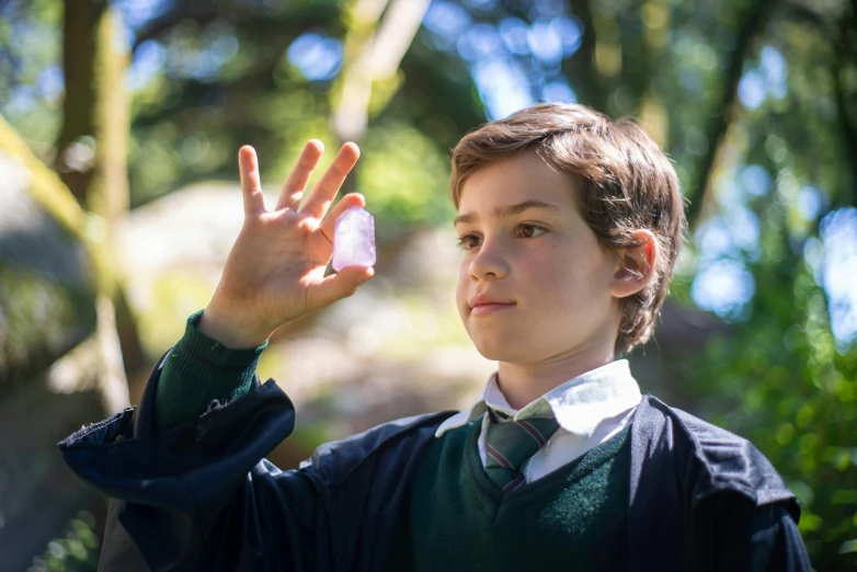 a young boy holding a pink object in his hand, inspired by Robert Alwyn Hughes, unsplash, outside the'school of magic ', presenting magic gem, cast, environmental shot