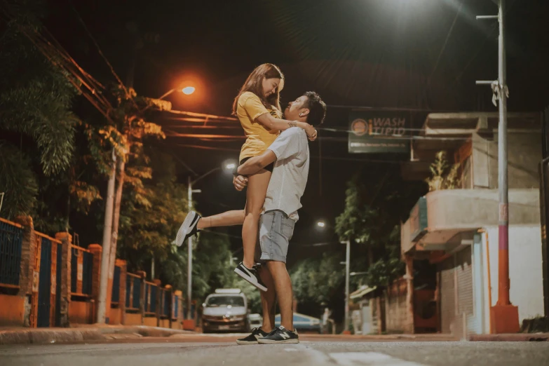 a man holding a woman in the middle of a street at night, pexels contest winner, attractive girl, on the concrete ground, gif, ad image