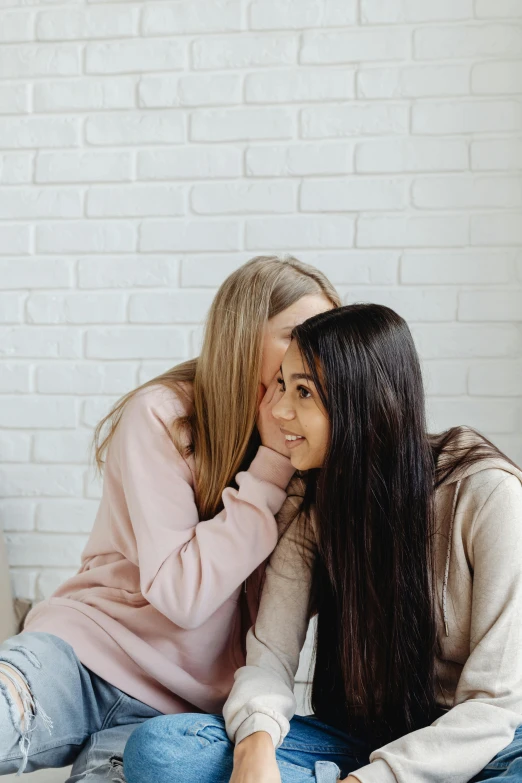 a couple of women sitting on top of a bed, trending on pexels, bite her lip, teenager, brown long and straight hair, hugs