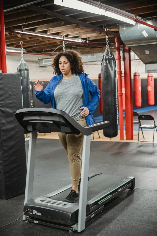 a woman on a treadie in a gym, happening, pacing, wearing a hoodie and sweatpants, square, medium-shot