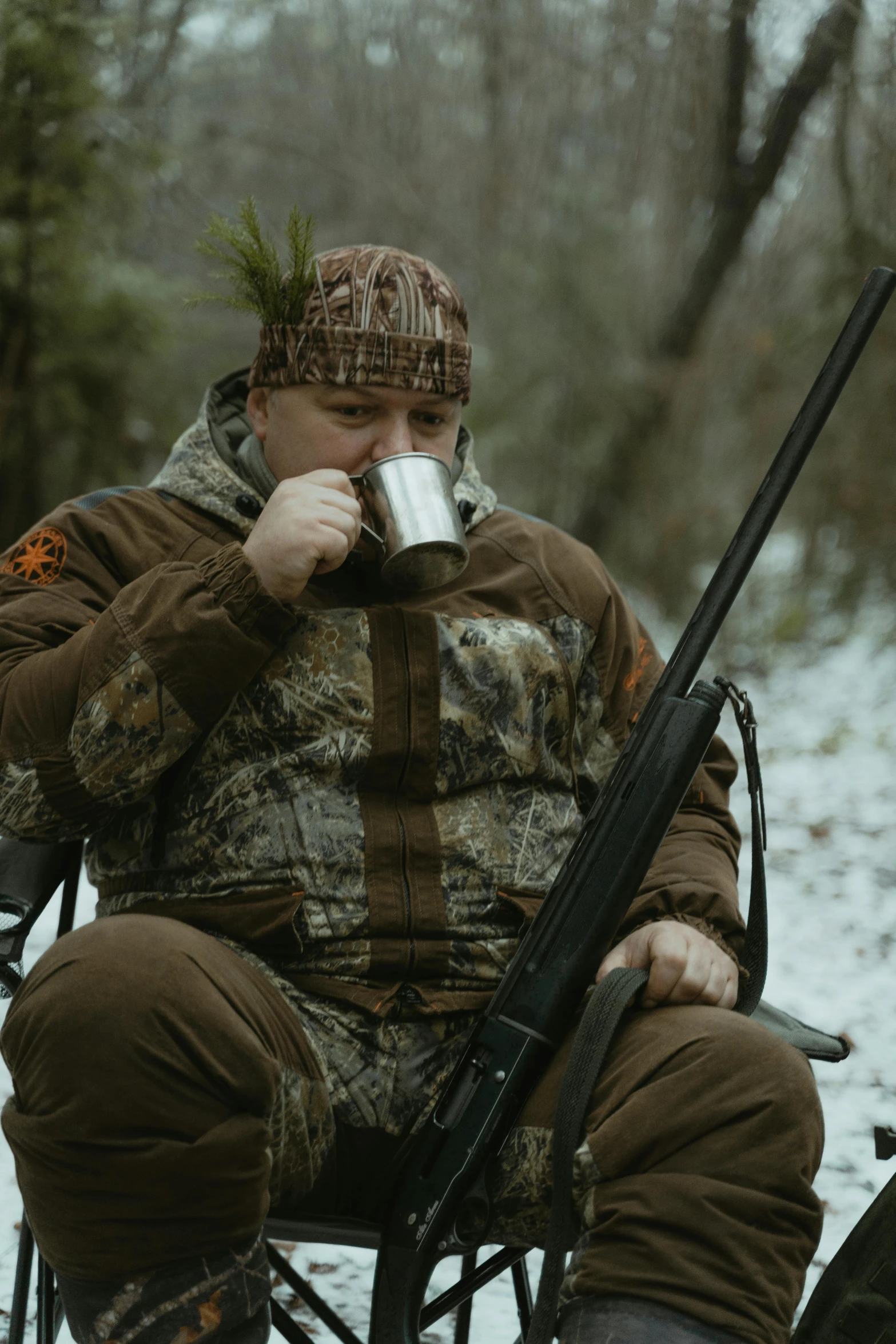a man sitting in a chair drinking from a cup, inspired by Brian 'Chippy' Dugan, trending on reddit, carrying a scoped hunting rifle, heavy winter aesthetics, political meeting in the woods, big toad