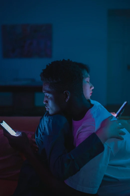 a man sitting on a couch looking at a cell phone, pexels, in the bedroom at a sleepover, twins playing video games, night time dark with neon colors, black teenage boy