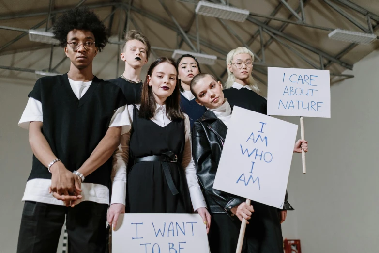 a group of people standing next to each other holding signs, trending on pexels, antipodeans, jean paul gaultier, male teenager, makeup, white and black clothing