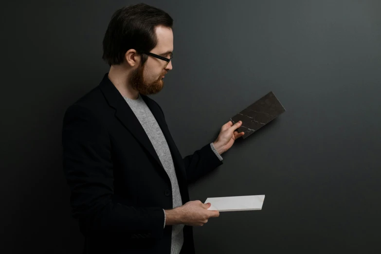 a man in a suit holding a piece of paper, inspired by David Chipperfield, dark matte metal, blacksmith product design, darkslategray wall, ricky berwick