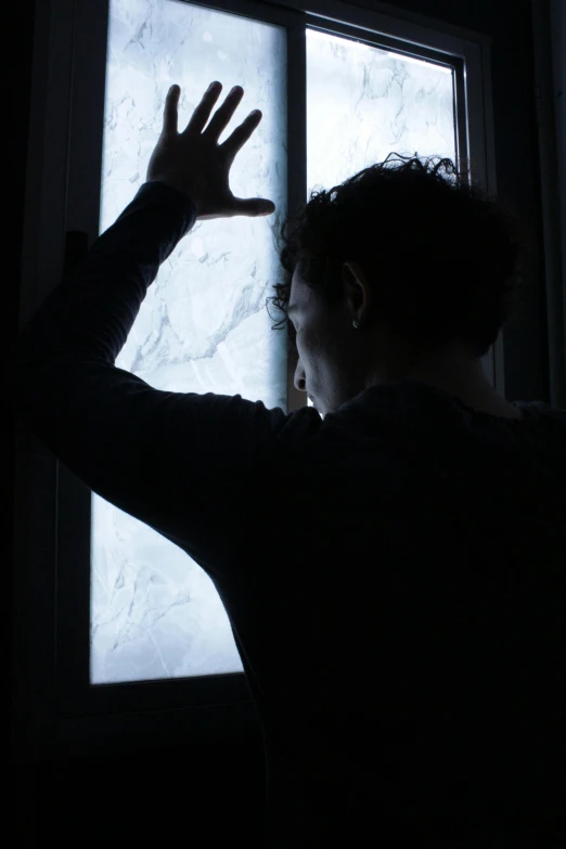 a person standing in front of a window in the dark, struggling, touching, frosted glass, worried