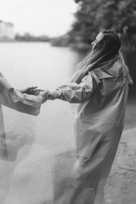 a black and white photo of two people holding hands, unsplash, romanticism, girl in raincoat, wearing flowing robes, joel fletcher, holding