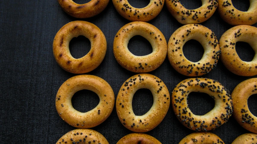a bunch of bagels sitting on top of a table, a portrait, trending on pexels, hurufiyya, black holes, middle eastern, dark bacgkground, a high angle shot