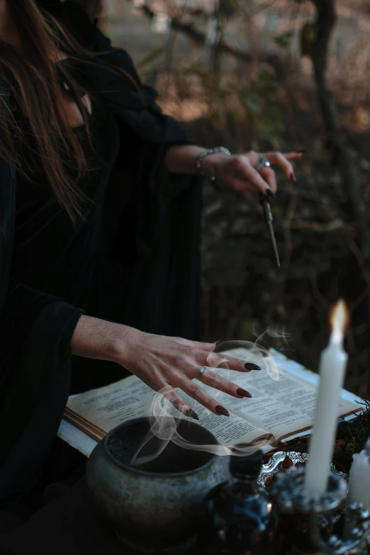 a woman sitting at a table with a book and a candle, wizard casting a spell, 2019 trending photo, wearing black robes, spells practice