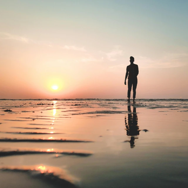 a man standing on top of a beach next to the ocean, pexels contest winner, minimalism, sun set, standing in shallow water, human staring blankly ahead, highly reflective