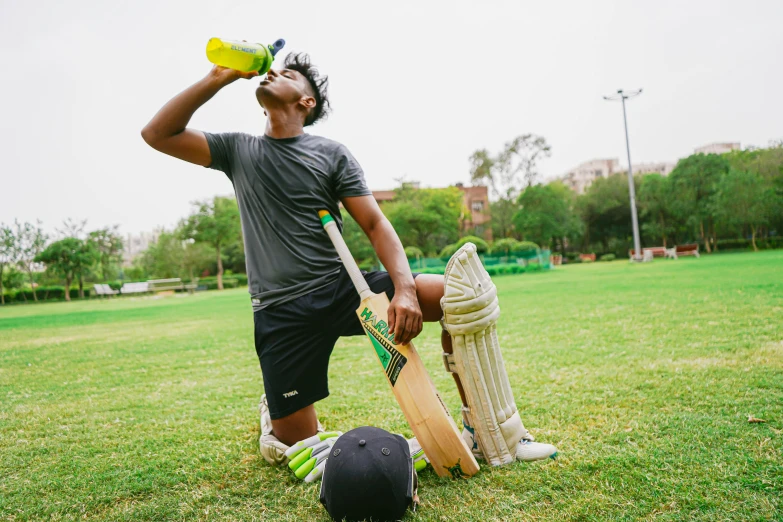 a man standing on top of a lush green field, girl drinks monster energy, neon yellow madhubani, athlete photography, holding bat