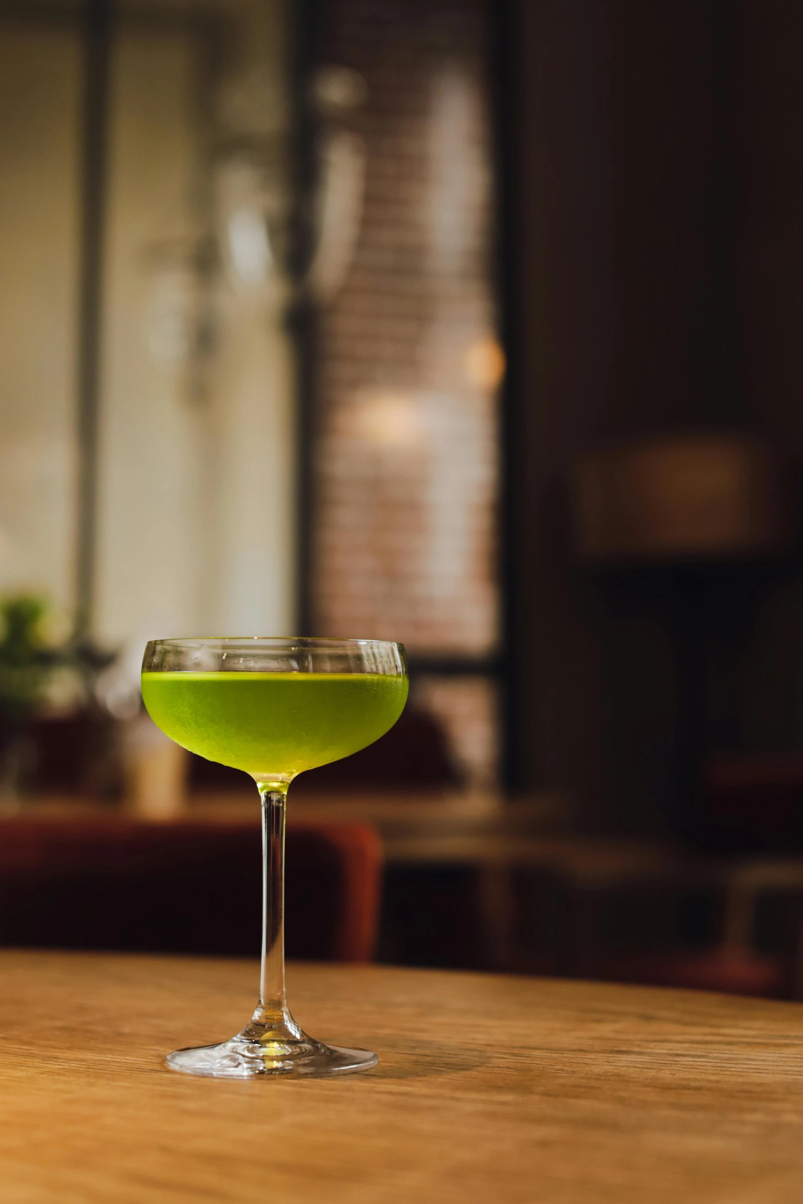 a green cocktail sitting on top of a wooden table, inspired by Ndoc Martini, renaissance, ignant, soft green natural light, f/4.5, new modern