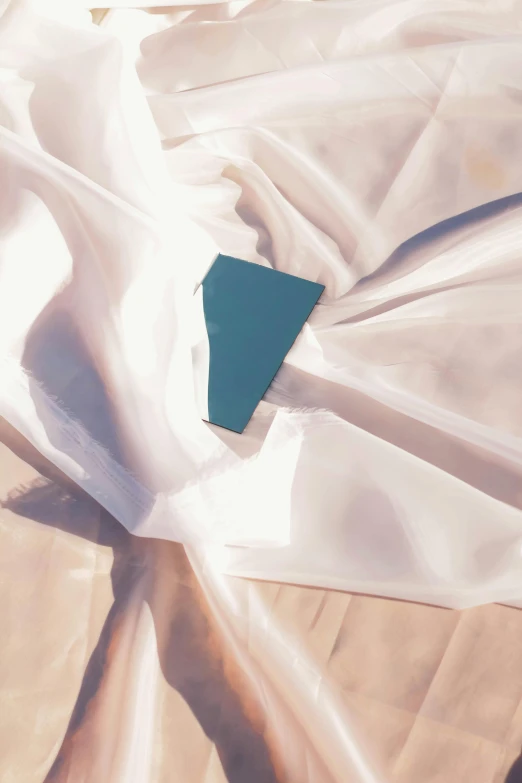 a book sitting on top of a bed covered in white sheets, an album cover, inspired by Raoul De Keyser, trending on unsplash, lyrical abstraction, white and teal garment, pearlescent skin, evening sunset, folds of fabric