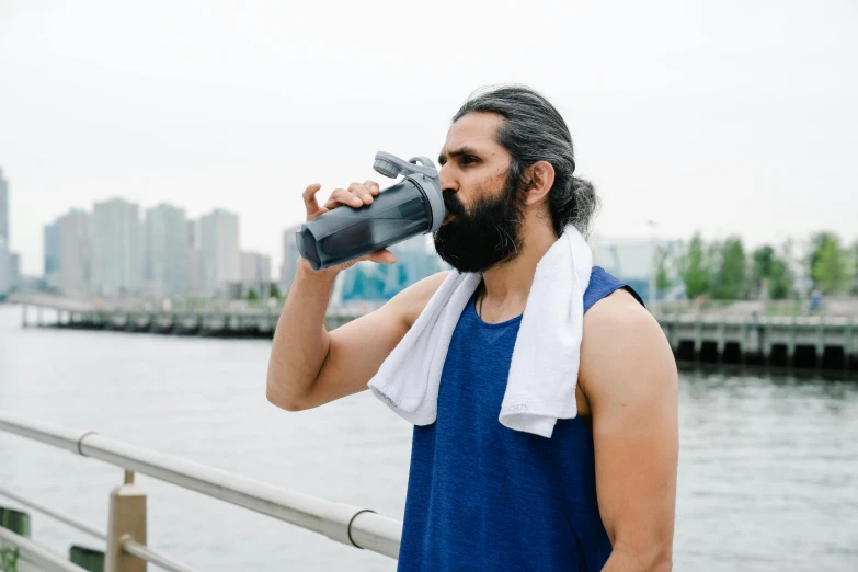 a man with a beard drinking from a water bottle, with a ponytail, steroid use, profile image, at the waterside