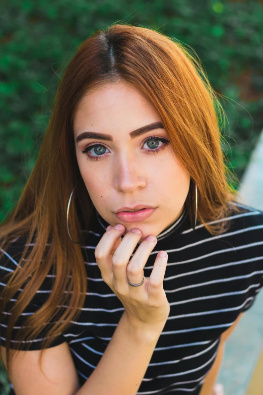 a woman sitting on a bench with her hand on her chin, inspired by Elsa Bleda, trending on pexels, photorealism, copper hair, wearing stripe shirt, beautiful huge eyes, wearing two metallic rings