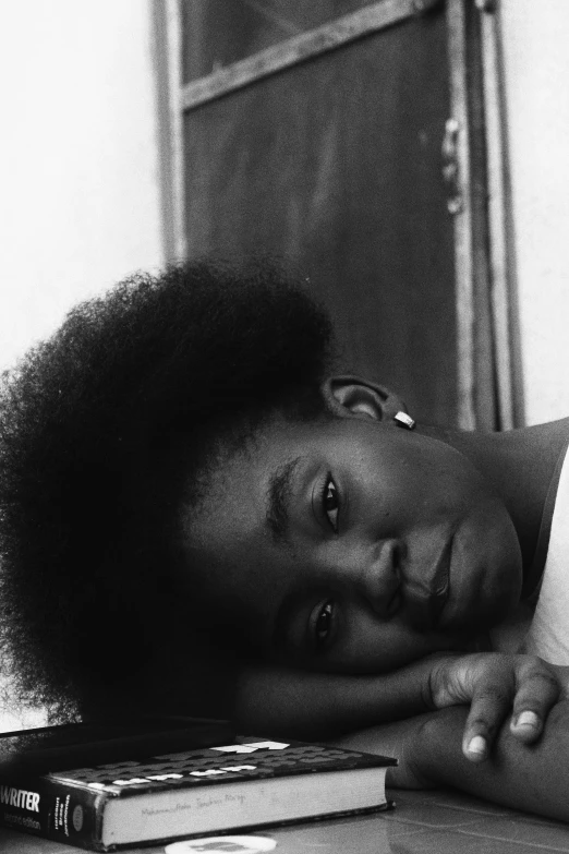 a woman laying on top of a pile of books, a black and white photo, inspired by Carrie Mae Weems, natural hair, ((portrait)), child, looking across the shoulder