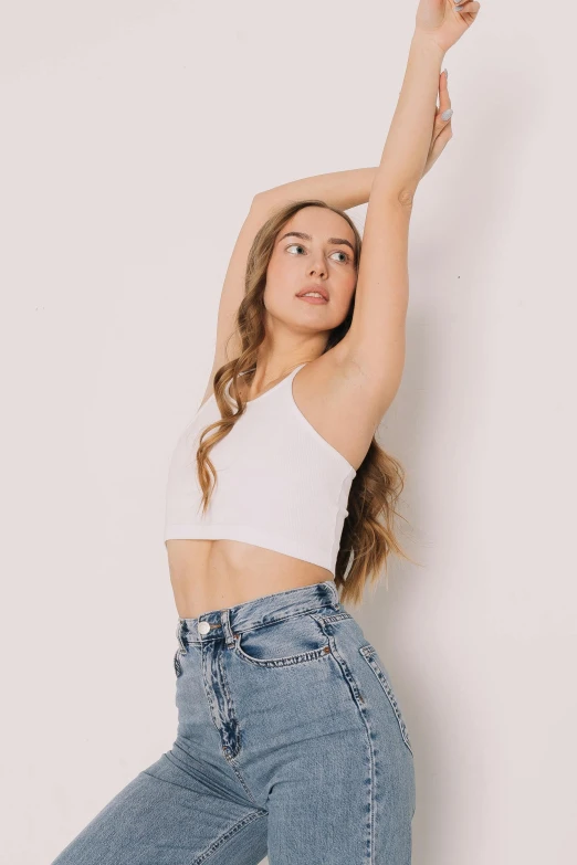 a woman in a white top and jeans leaning against a wall, trending on unsplash, wearing : tanktop, white background, portrait sophie mudd, wearing crop top