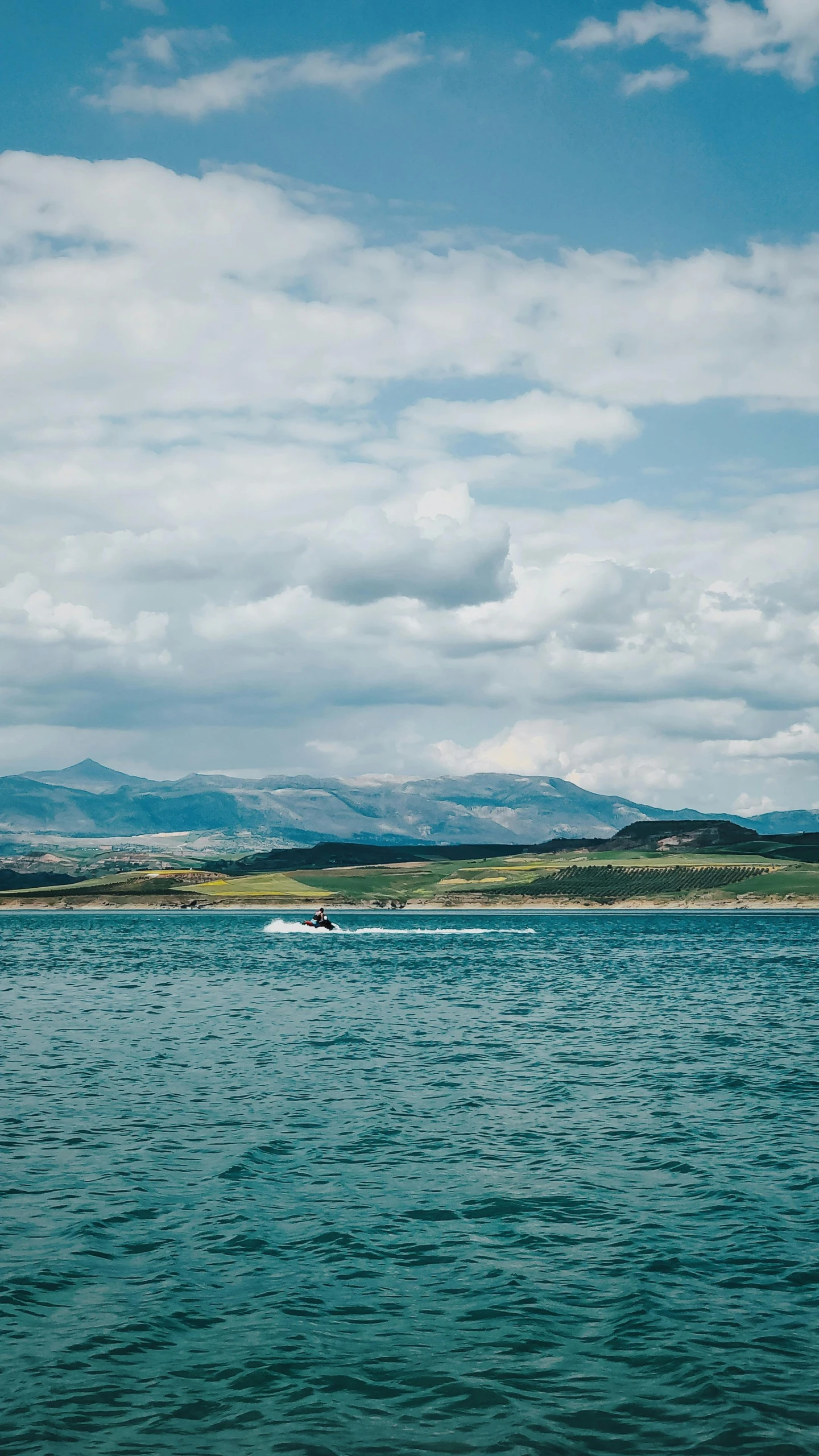 a boat traveling across a large body of water, by Andrew Allan, unsplash, hills in the background, high quality photo, big sky, van