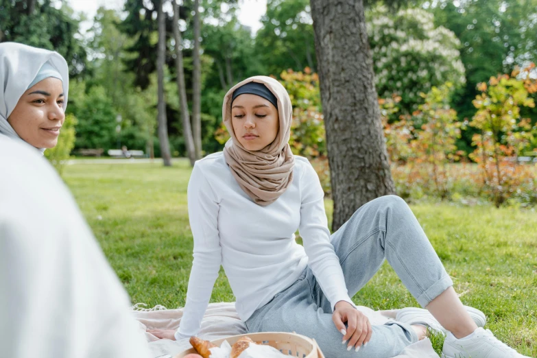 a couple of women sitting on top of a grass covered field, trending on pexels, hurufiyya, people inside eating meals, white scarf, a park, animated