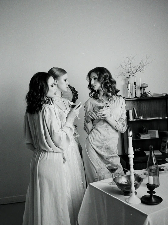 a couple of women standing next to each other near a table, a black and white photo, by Zofia Stryjenska, unsplash, renaissance, drinking champagne, wearing a nightgown, three women, abigail larson