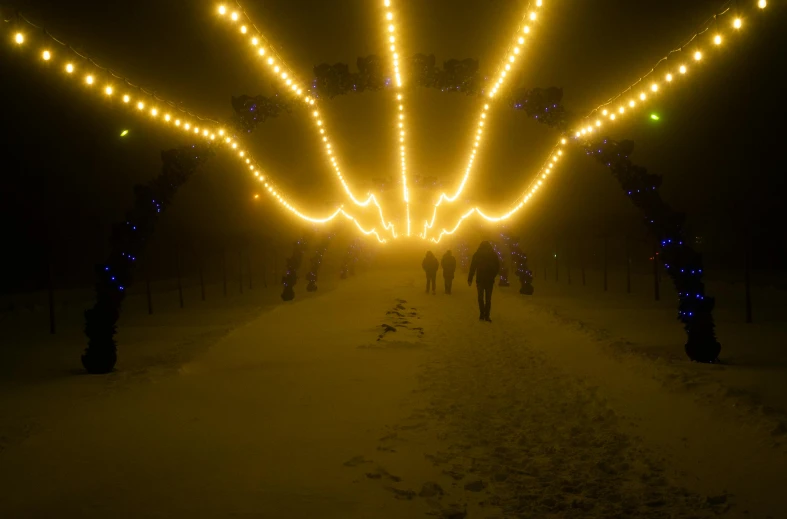 a group of people walking down a snow covered road, unsplash contest winner, land art, concert lights, ornamental halo, yellow volumetric fog, christmas night