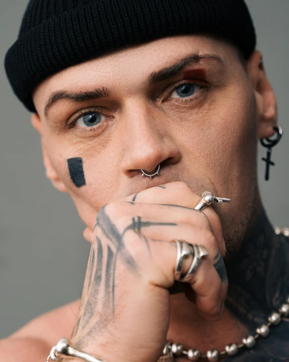 a close up of a person with tattoos on his face, inspired by Seb McKinnon, trending on pexels, antipodeans, nonbinary model, in style of chrome hearts, point finger with ring on it, pouty face