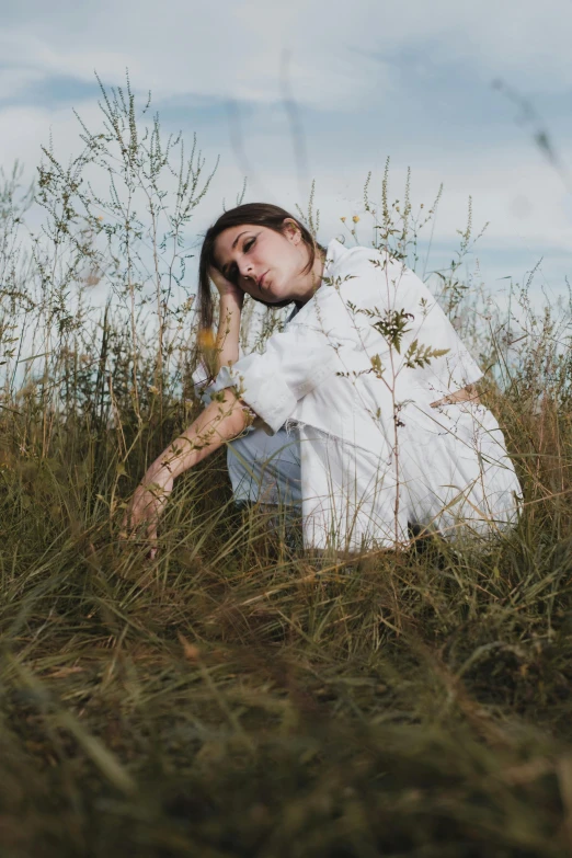 a woman sitting in a field of tall grass, an album cover, inspired by Elsa Bleda, renaissance, wearing a white shirt, thoughtful pose, high quality photo, on the ground