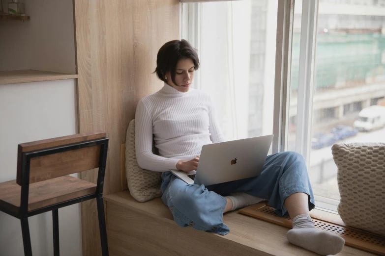 a woman sitting on a window sill using a laptop, trending on pexels, white shirt and jeans, sitting in a lounge, busy, louise zhang