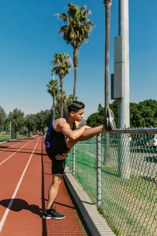 a man leaning over a fence on a track, by Robbie Trevino, dynamic stretching, with palm trees in the back, university, profile image