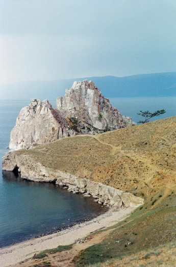 a horse standing on top of a hill next to a body of water, an album cover, inspired by Konstantin Vasilyev, 1960s color photograph, chiseled formations, overview, kazakh empress