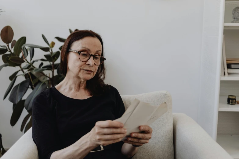 a woman sitting on a couch reading a book, a photo, by Emma Andijewska, pexels contest winner, white reading glasses, dementia, avatar image, on a white table