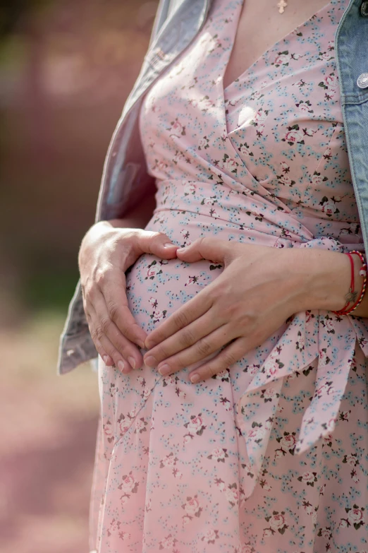 a pregnant woman wearing a pink dress and denim jacket, pexels, patterned, birth, her hand is on her waist, outdoor photo