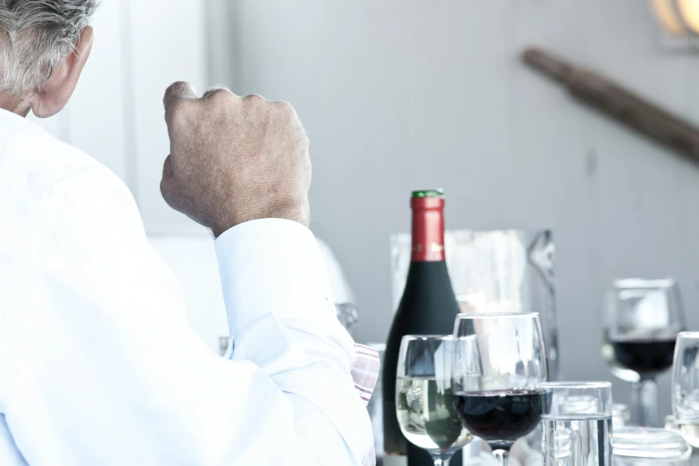 a man sitting at a table with a bottle of wine, unsplash, shrugging arms, close up shot from the side, white sleeves, colour corrected