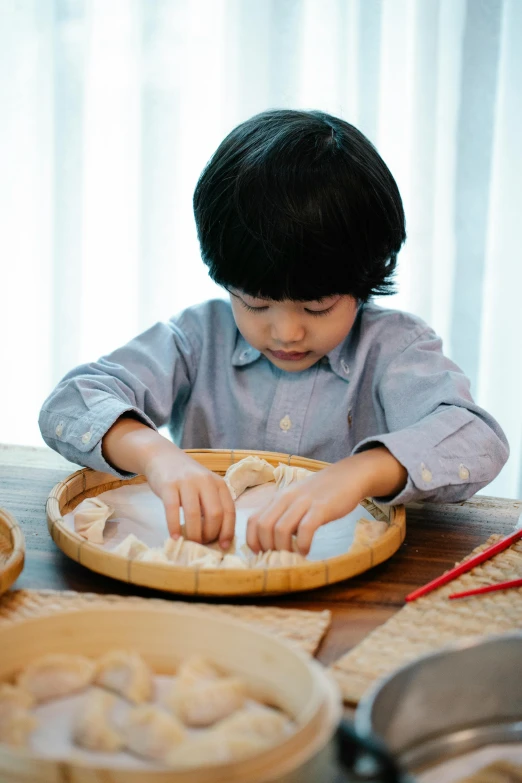 a little boy that is sitting at a table, inspired by Li Di, pexels contest winner, process art, dumplings on a plate, made of bamboo, japanese collection product, singapore