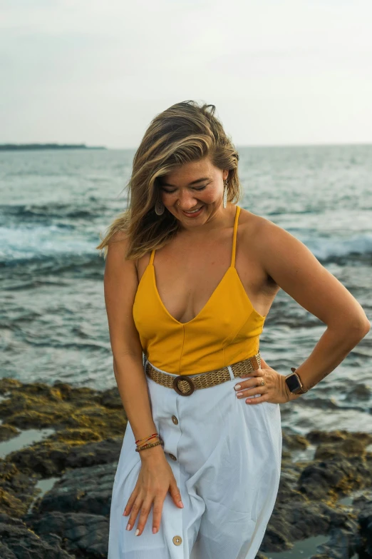 a woman standing on a rocky beach next to the ocean, wearing yellow croptop, sydney sweeney, headshot profile picture, profile image