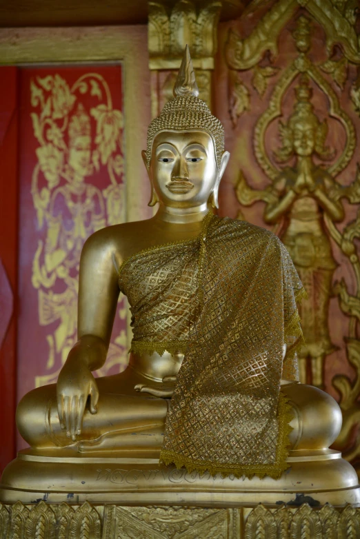 a golden buddha statue sitting in front of a red wall, royal palace interior, square, nivanh chanthara, medium-shot