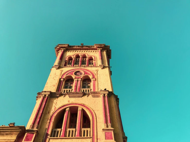 a tall clock tower with a blue sky in the background, inspired by Wes Anderson, pexels contest winner, bengal school of art, faded colors, pink and yellow, bangalore, multiple stories