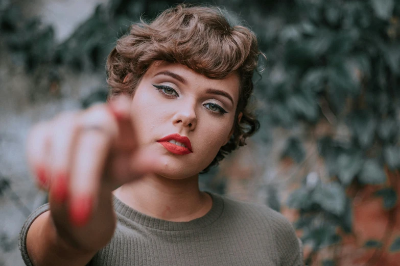 a woman pointing her finger at the camera, inspired by Elsa Bleda, trending on pexels, magic realism, curly pixie cut hair, retro pinup model, lipstick, teenage girl