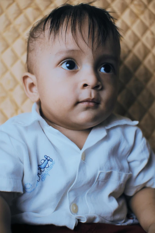 a close up of a baby sitting on a bed, an album cover, by Basuki Abdullah, wearing a white button up shirt, blue eyed, vinayak, serious and stern expression