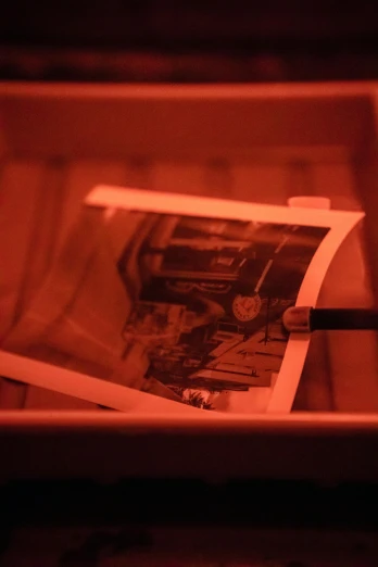 a picture is being taken out of an oven, a photocopy, inspired by Nan Goldin, unsplash, holography, in a wooden box. top down photo, red tint, ambient amber light, an ultrafine detailed photo