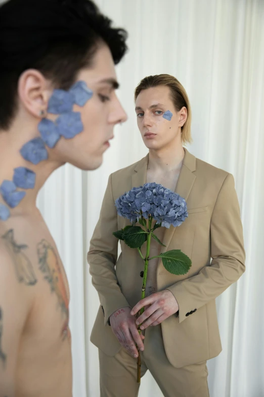 a man standing next to a woman holding a flower, unsplash, aestheticism, huge earrings and queer make up, alex kanevsky, blue flowers, lean man with light tan skin