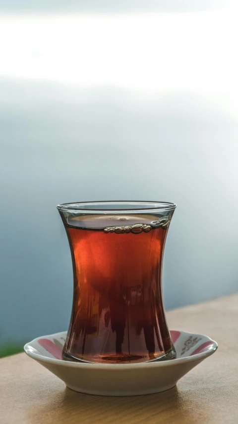 a cup of tea sitting on top of a wooden table, by Yasar Vurdem, pexels, hurufiyya, tansparent water, brown red blue, port, portrait n - 9