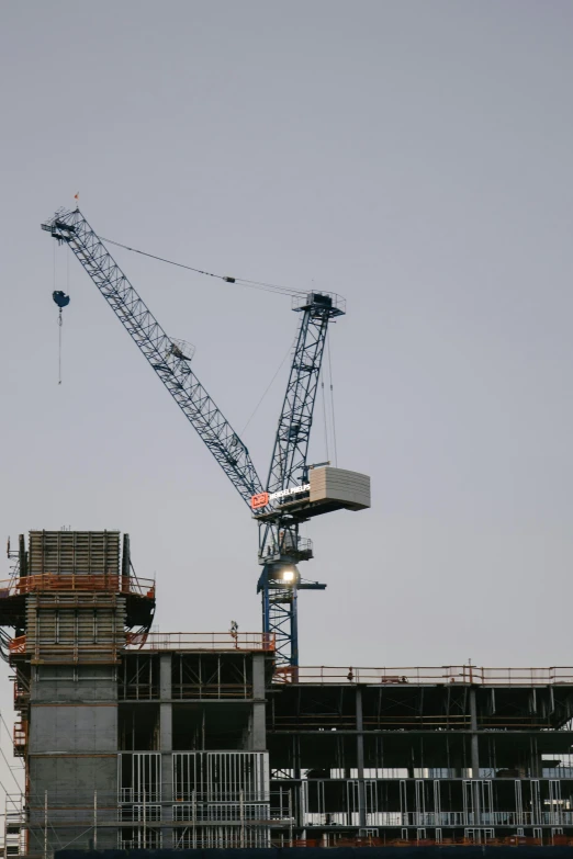 a crane standing on top of a building under construction, by Dave Allsop, flickr, zoomed out, promo image, sitting, hi-res