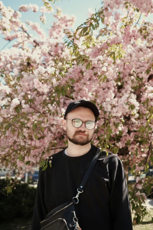 a man standing in front of a flowering tree, by Attila Meszlenyi, unsplash, portrait of sam hyde, low quality photo, dasha taran, non-binary